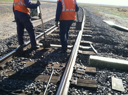 two people wearing safety vests and holding shovels stand on train tracks